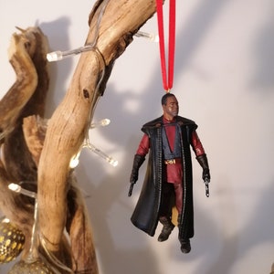 K&ouml;nnte beinhalten: Ein schwarzer und roter Weihnachtsbaumschmuck mit einer Figur aus einem Science-Fiction-Film. Der Schmuck h&auml;ngt an einem Zweig mit einem roten Band.