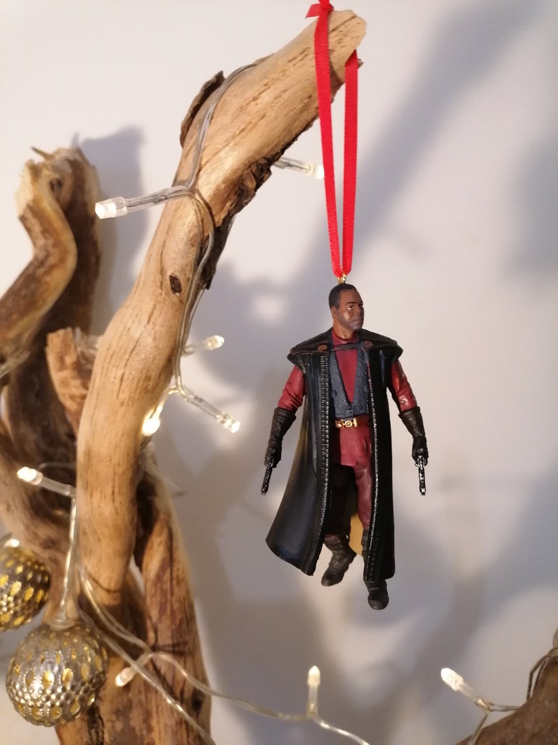 K&ouml;nnte beinhalten: Ein schwarzer und roter Weihnachtsbaumschmuck mit einer Figur aus einem Science-Fiction-Film. Der Schmuck h&auml;ngt an einem Zweig mit einem roten Band.