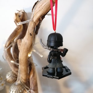 May include: Black and red Star Wars ornament featuring Kylo Ren with a lightsaber. The ornament is hanging from a red ribbon on a branch.