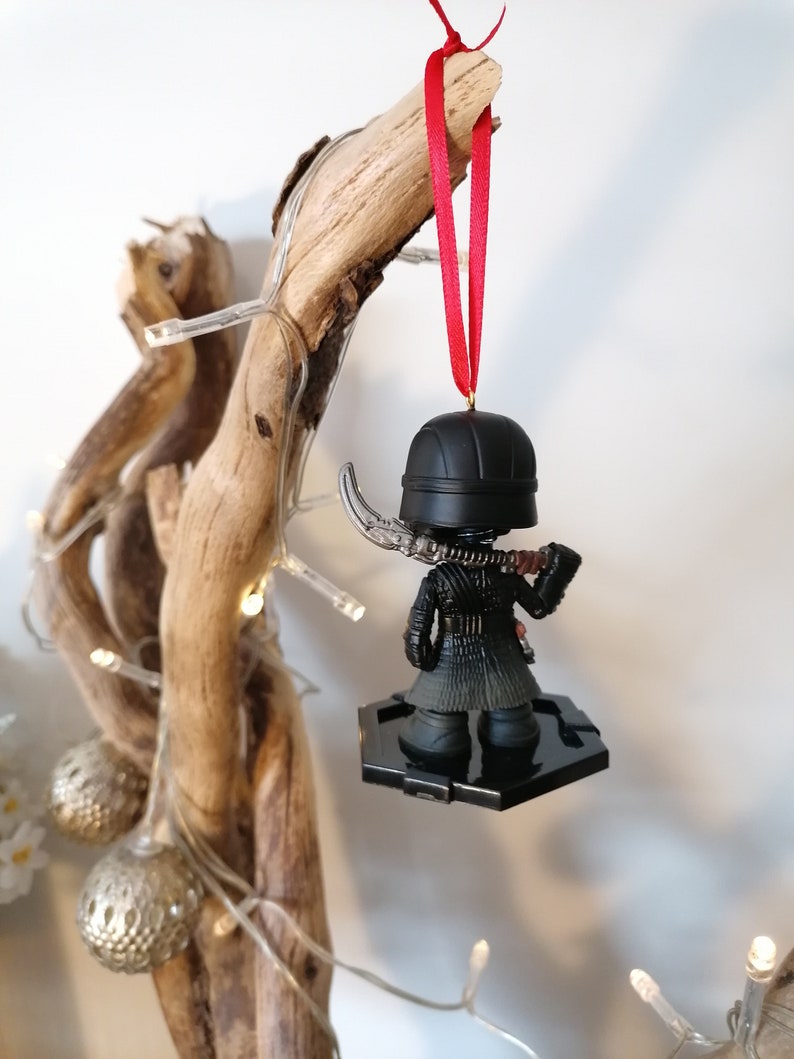 May include: Black and red Star Wars ornament featuring Kylo Ren with a lightsaber. The ornament is hanging from a red ribbon on a branch.