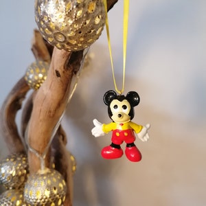 K&ouml;nnte beinhalten: Eine gelbe Schnur h&auml;ngt an einem Ast mit einem kleinen Mickey Mouse-Anh&auml;nger aus Plastik. Der Anh&auml;nger ist schwarz, gelb und rot.