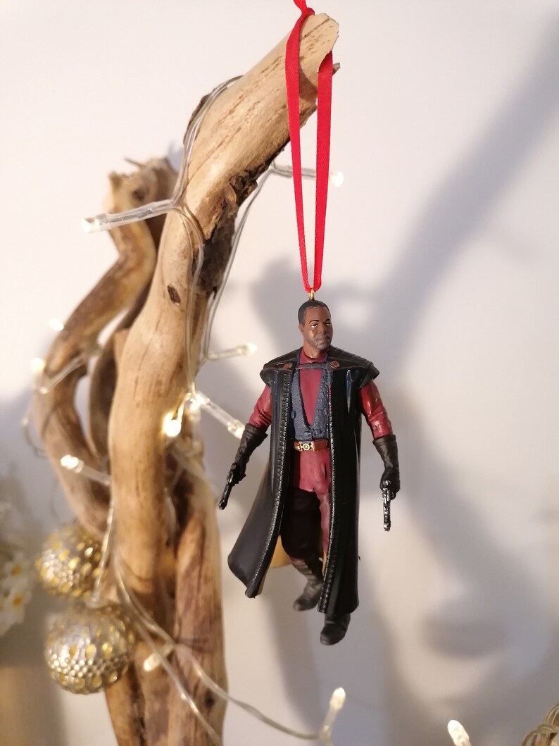 K&ouml;nnte beinhalten: Ein schwarzer und roter Star Wars-Charakter-Anh&auml;nger mit einem roten Band, das an einem Ast h&auml;ngt.