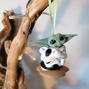 K&ouml;nnte beinhalten: Ein gr&uuml;ner und wei&szlig;er Weihnachtsbaumschmuck mit einer Figur aus dem Star Wars-Franchise. Die Figur sitzt in einer wei&szlig;en Kapsel mit braunem Sockel.