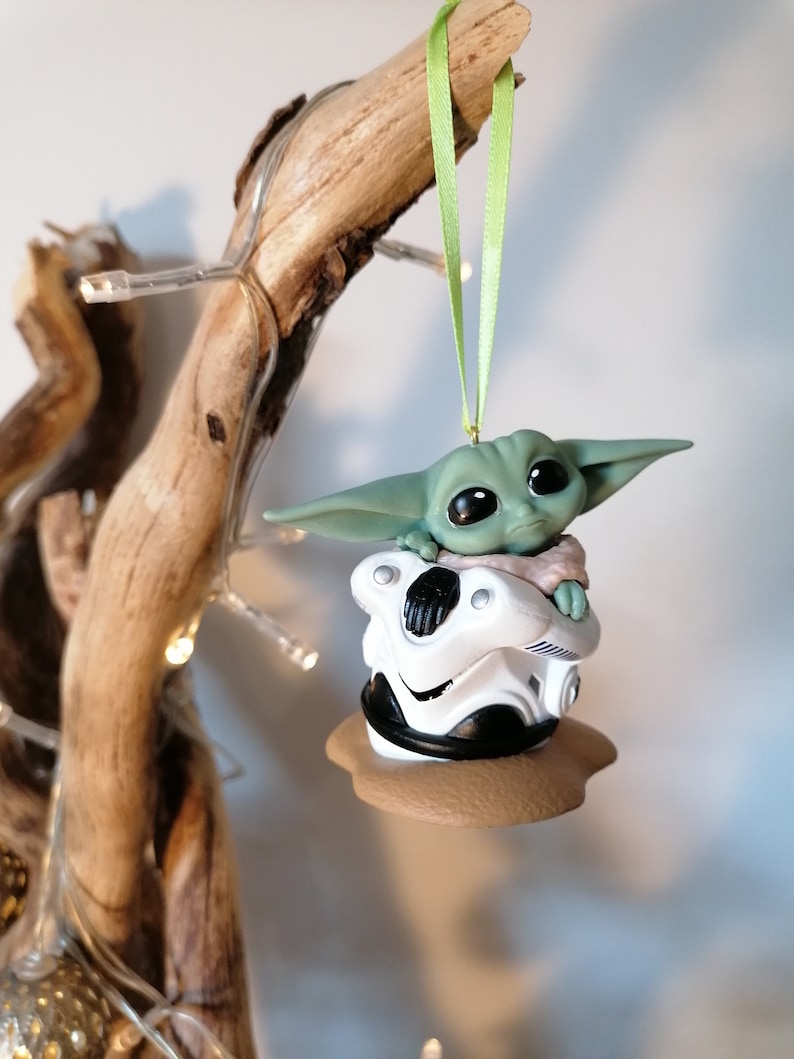 K&ouml;nnte beinhalten: Ein gr&uuml;ner und wei&szlig;er Weihnachtsbaumschmuck mit einer Figur aus dem Star Wars-Franchise. Die Figur sitzt in einer wei&szlig;en Kapsel mit braunem Sockel.