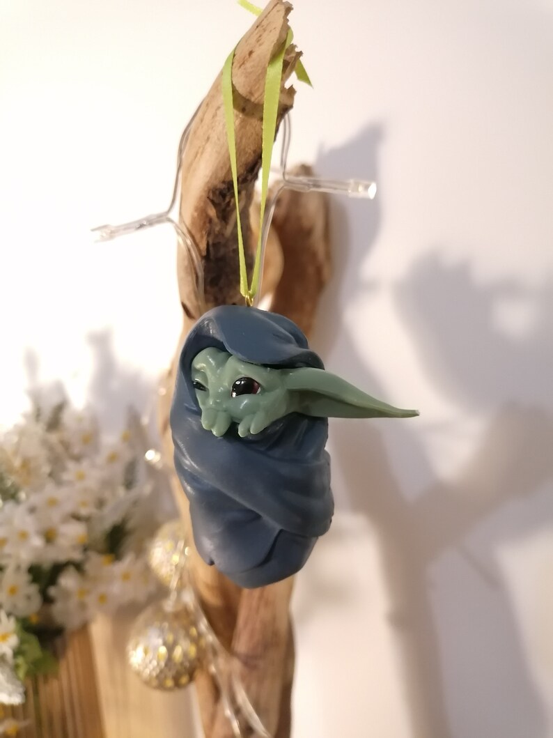 May include: A green and blue Christmas ornament featuring a character from the Star Wars franchise, wrapped in a blue blanket.