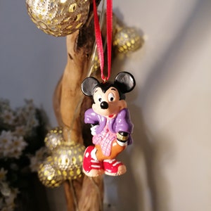 K&ouml;nnte beinhalten: Ein violetter und rosa Mickey Mouse Weihnachtsbaumschmuck mit einem roten Band, das an einem Ast h&auml;ngt.