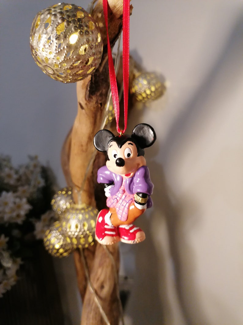 K&ouml;nnte beinhalten: Ein violetter und rosa Mickey Mouse Weihnachtsbaumschmuck mit einem roten Band, das an einem Ast h&auml;ngt.