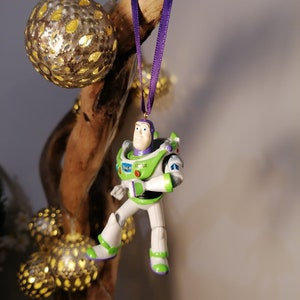 May include: A green and white Buzz Lightyear Christmas ornament with a purple ribbon hanging from a branch.