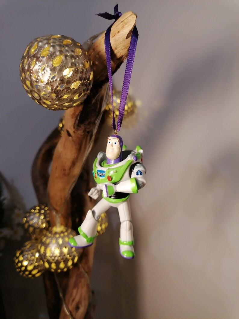 May include: A green and white Buzz Lightyear Christmas ornament with a purple ribbon hanging from a branch.