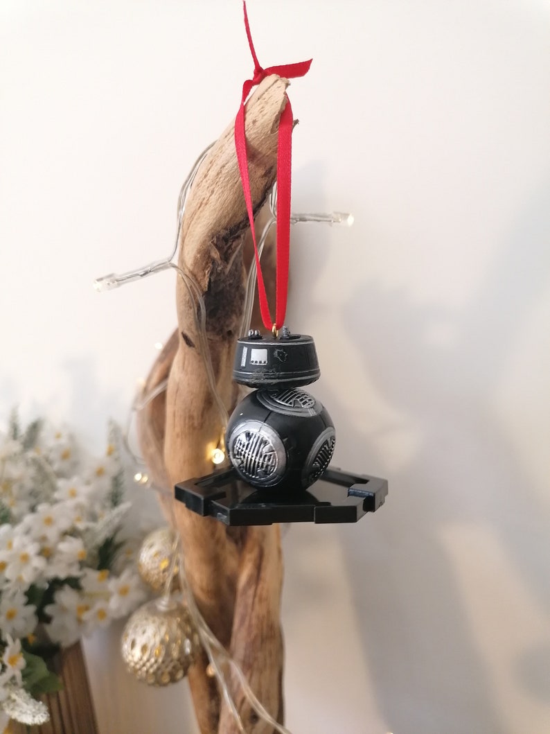 K&ouml;nnte beinhalten: Schwarzer und silberner Star Wars BB-8 Weihnachtsbaumschmuck mit einem roten Band, das an einem St&uuml;ck Treibholz h&auml;ngt.