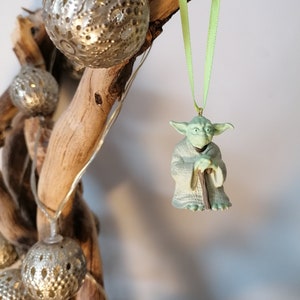 May include: Green Yoda Christmas ornament with a green ribbon hanging from a branch with silver and white decorative balls.