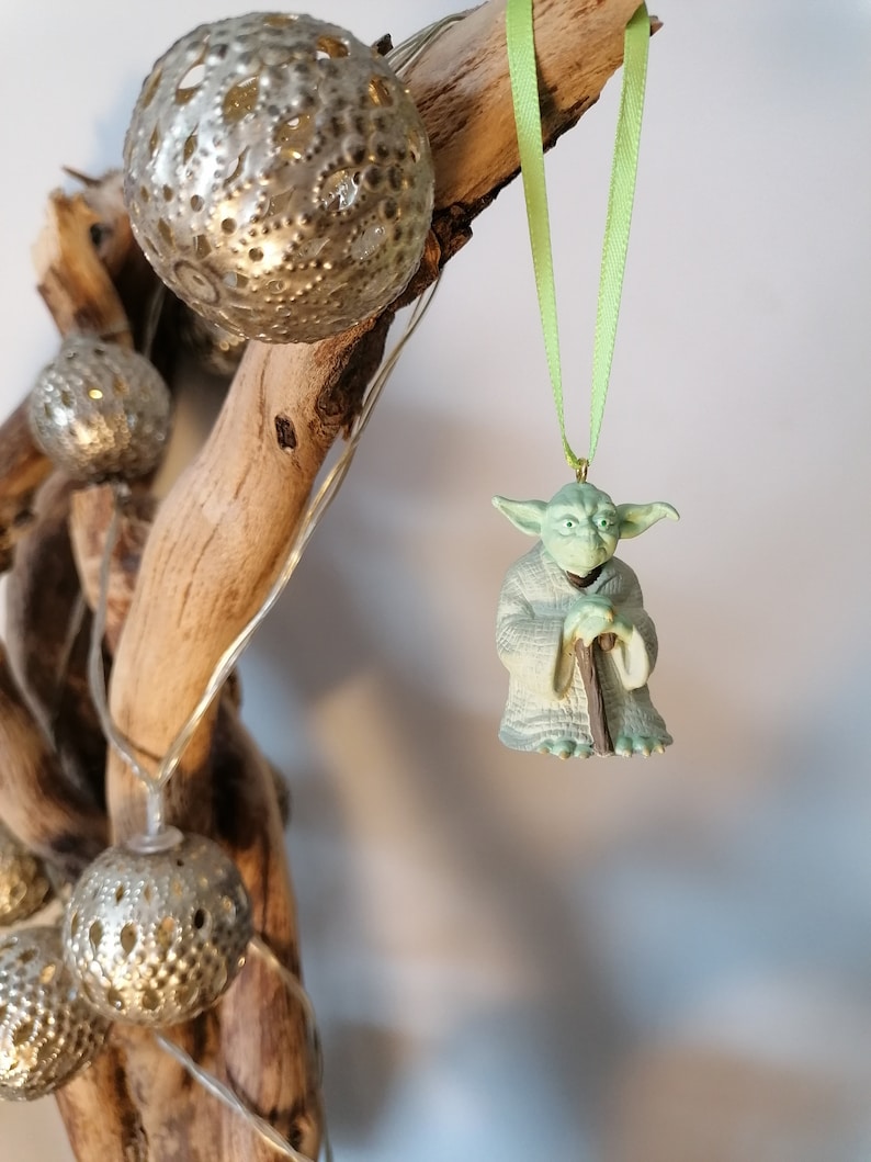 May include: Green Yoda Christmas ornament with a green ribbon hanging from a branch with silver and white decorative balls.
