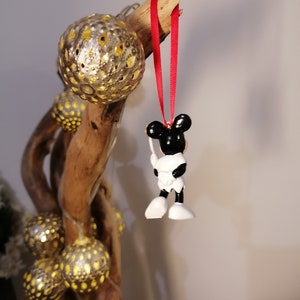 May include: A black and white Mickey Mouse ornament with a red ribbon hanging from a branch with gold and yellow ornaments.