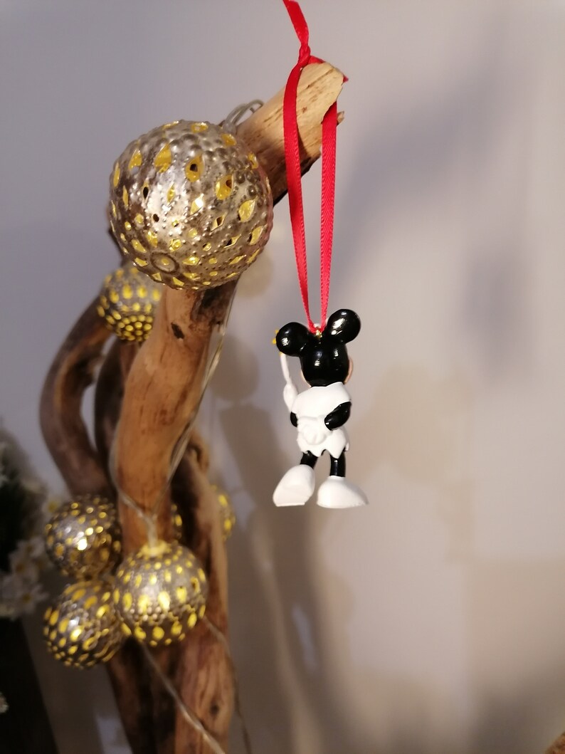 May include: A black and white Mickey Mouse ornament with a red ribbon hanging from a branch with gold and yellow ornaments.