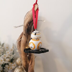 May include: A white and orange Star Wars BB-8 character ornament with a red ribbon hanging from a driftwood branch.