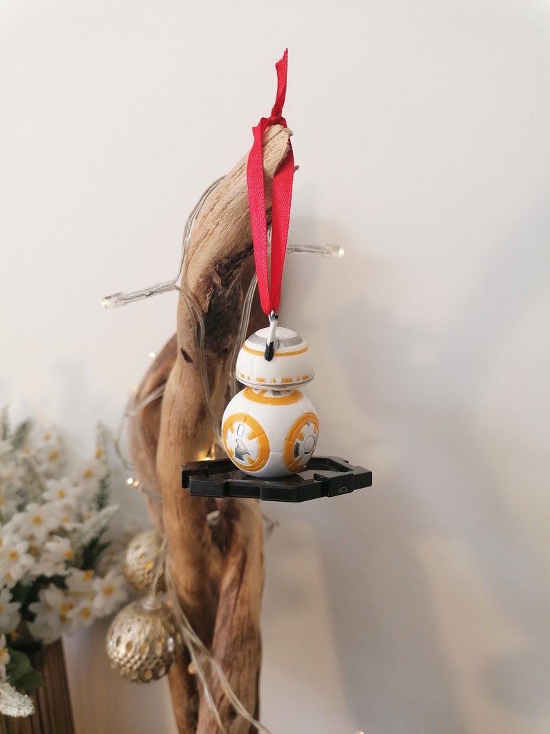 May include: A white and orange Star Wars BB-8 character ornament with a red ribbon hanging from a driftwood branch.