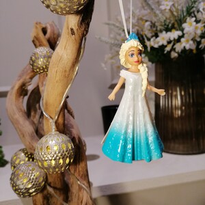 Peut inclure: Une figurine de princesse blanche et bleue avec des cheveux blonds et une couronne bleue. La poup&eacute;e est suspendue &agrave; une ficelle blanche sur une branche avec des ampoules dor&eacute;es.