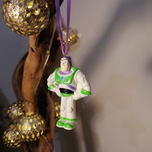 Puede incluir: Una figura de juguete de pl&aacute;stico de Buzz Lightyear de la franquicia Toy Story. La figura lleva su traje de ranger espacial caracter&iacute;stico, con un chaleco verde, un traje espacial blanco y detalles morados. La figura est&aacute; colgada de una cinta morada.