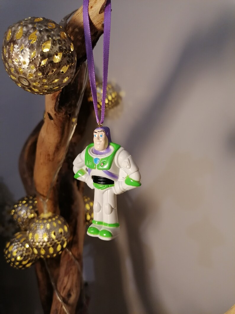 Puede incluir: Una figura de juguete de pl&aacute;stico de Buzz Lightyear de la franquicia Toy Story. La figura lleva su traje de ranger espacial caracter&iacute;stico, con un chaleco verde, un traje espacial blanco y detalles morados. La figura est&aacute; colgada de una cinta morada.
