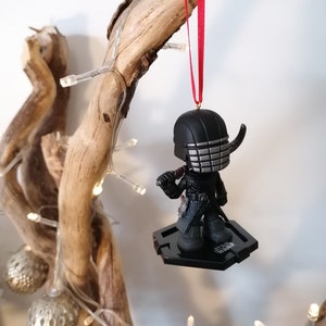 May include: Black and silver Star Wars ornament featuring Kylo Ren with a red ribbon.