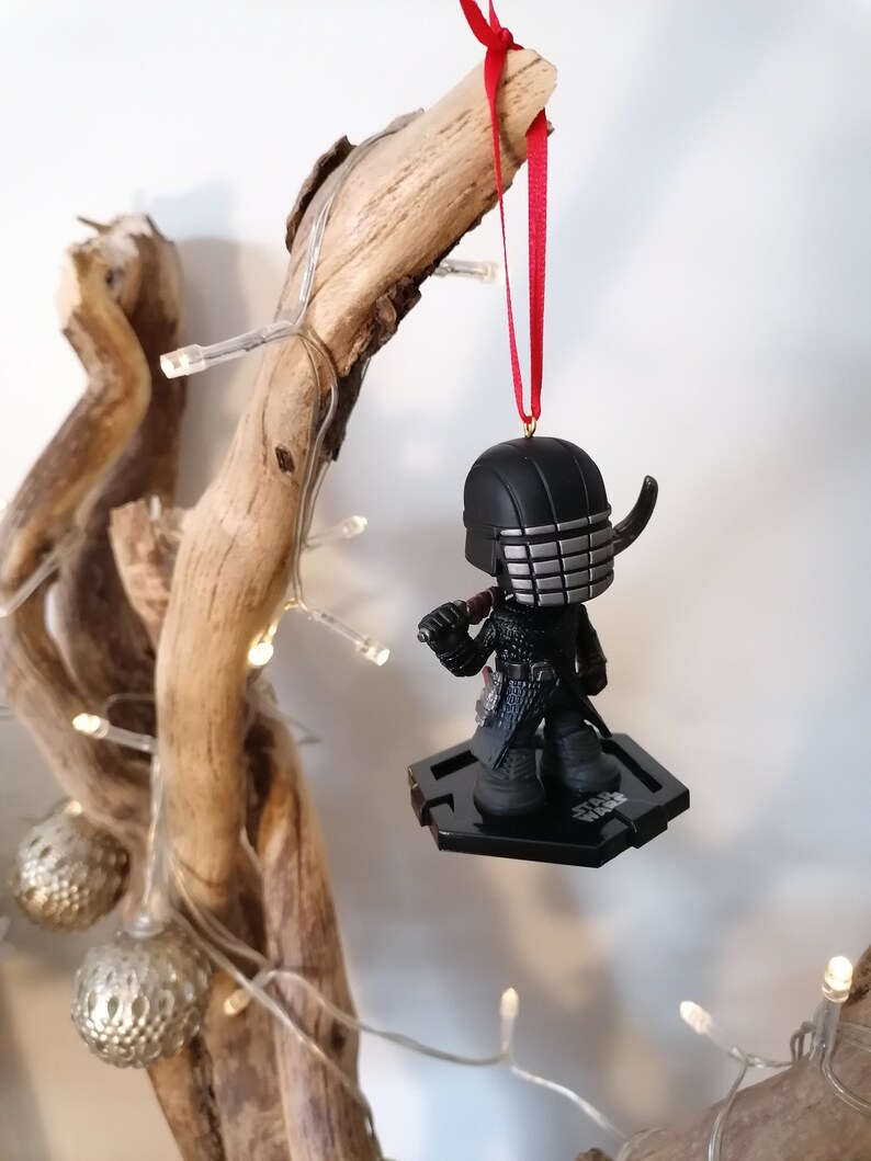 May include: Black and silver Star Wars ornament featuring Kylo Ren with a red ribbon.