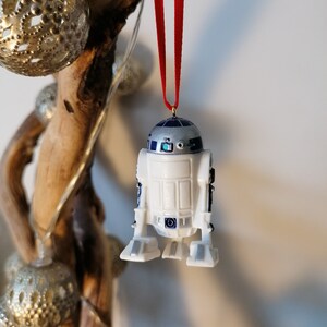 K&ouml;nnte beinhalten: Ein wei&szlig;er und blauer R2-D2 Weihnachtsbaumschmuck mit einem roten Band. Der Schmuck ist aus Kunststoff und hat ein detailliertes Design.