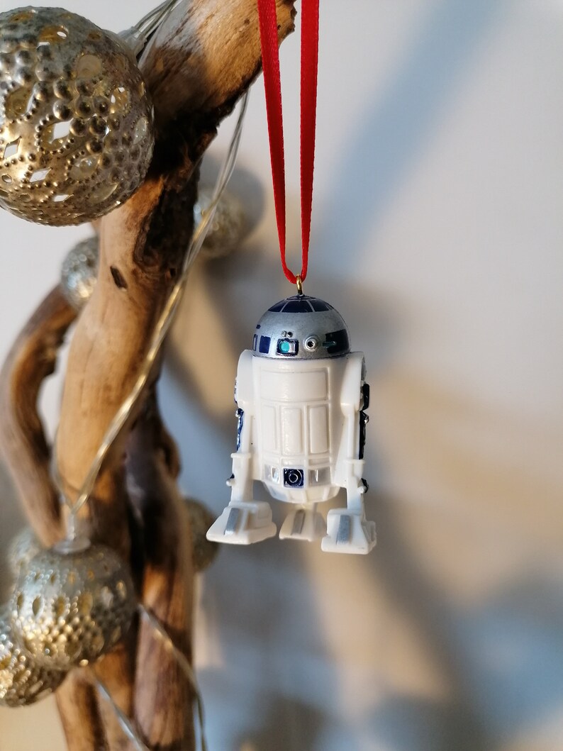 K&ouml;nnte beinhalten: Ein wei&szlig;er und blauer R2-D2 Weihnachtsbaumschmuck mit einem roten Band. Der Schmuck ist aus Kunststoff und hat ein detailliertes Design.