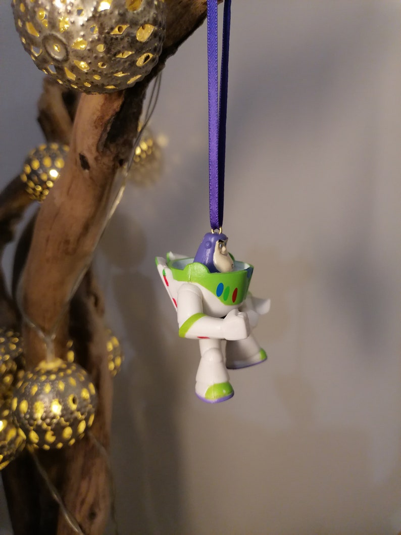 May include: A white and green Buzz Lightyear Christmas ornament with a purple ribbon hanging from a branch.