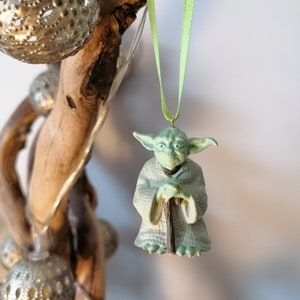 May include: A green Yoda ornament with a brown staff hanging from a green ribbon on a branch.