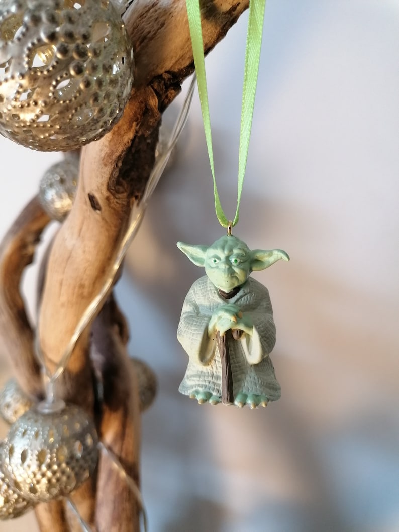 May include: A green Yoda ornament with a brown staff hanging from a green ribbon on a branch.