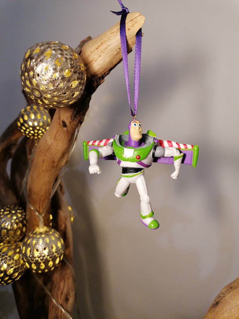 May include: A purple and green plastic toy figurine of Buzz Lightyear from the Toy Story movie franchise. The figurine is hanging from a purple ribbon and has wings.