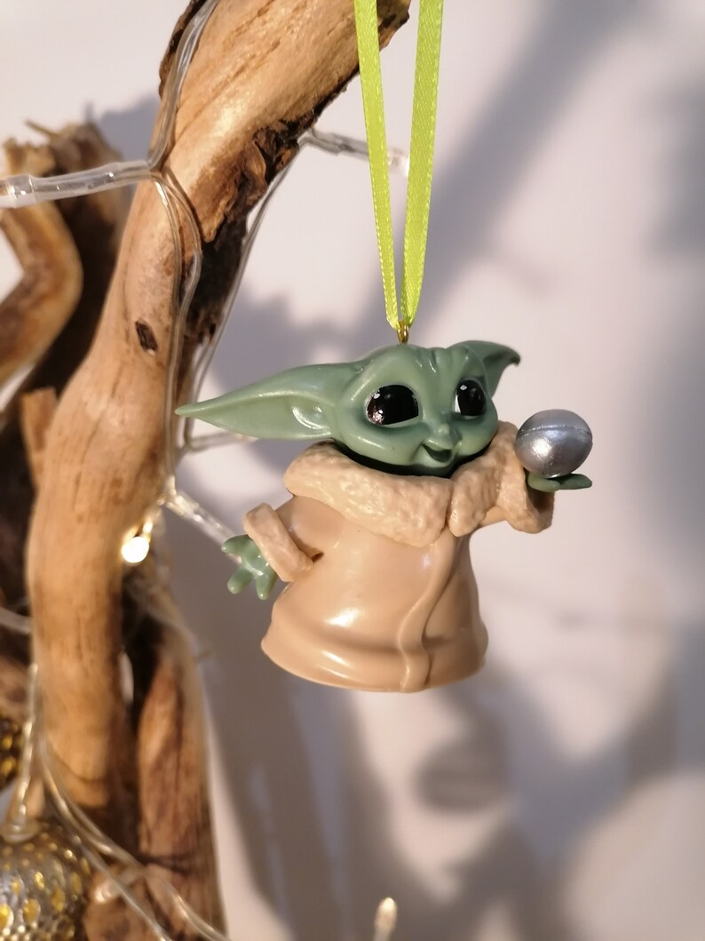 May include: A green and brown Christmas ornament featuring a character from the Star Wars franchise, holding a silver ball.