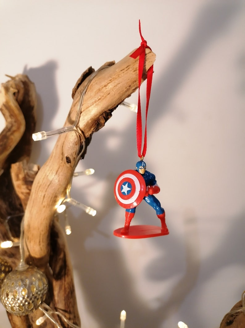 May include: A red, white, and blue Captain America Christmas ornament with a red ribbon hanging from a branch.
