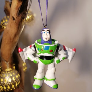 Pu&ograve; includere: Un ornamento di plastica verde, bianco e viola di Buzz Lightyear del franchise Toy Story. Indossa la sua tuta da ranger spaziale e ha un'espressione seria sul viso.