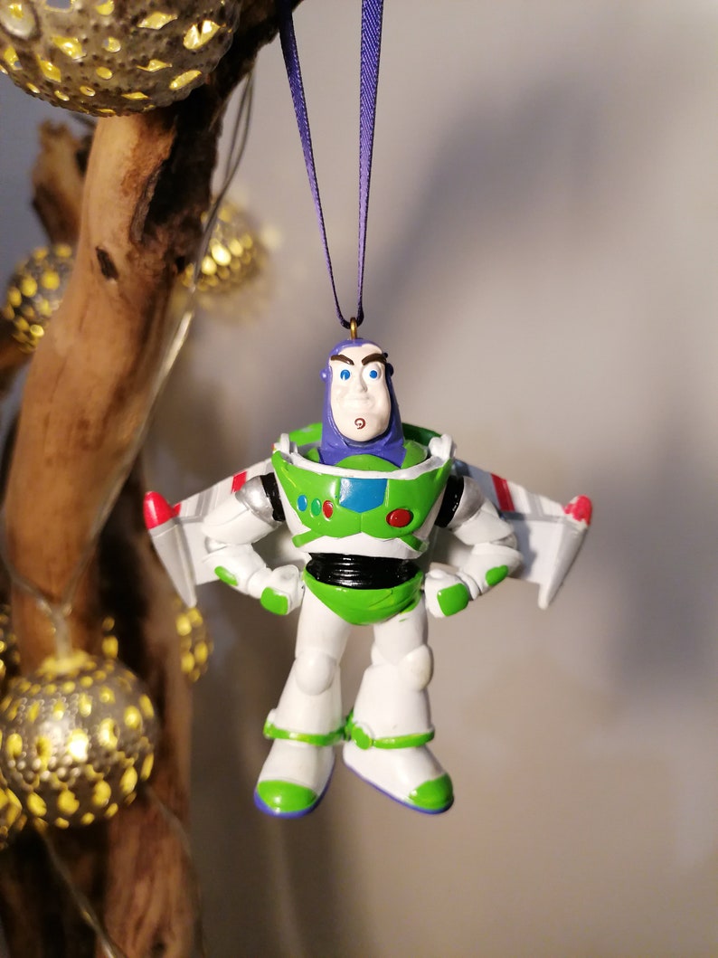 Pu&ograve; includere: Un ornamento di plastica verde, bianco e viola di Buzz Lightyear del franchise Toy Story. Indossa la sua tuta da ranger spaziale e ha un'espressione seria sul viso.