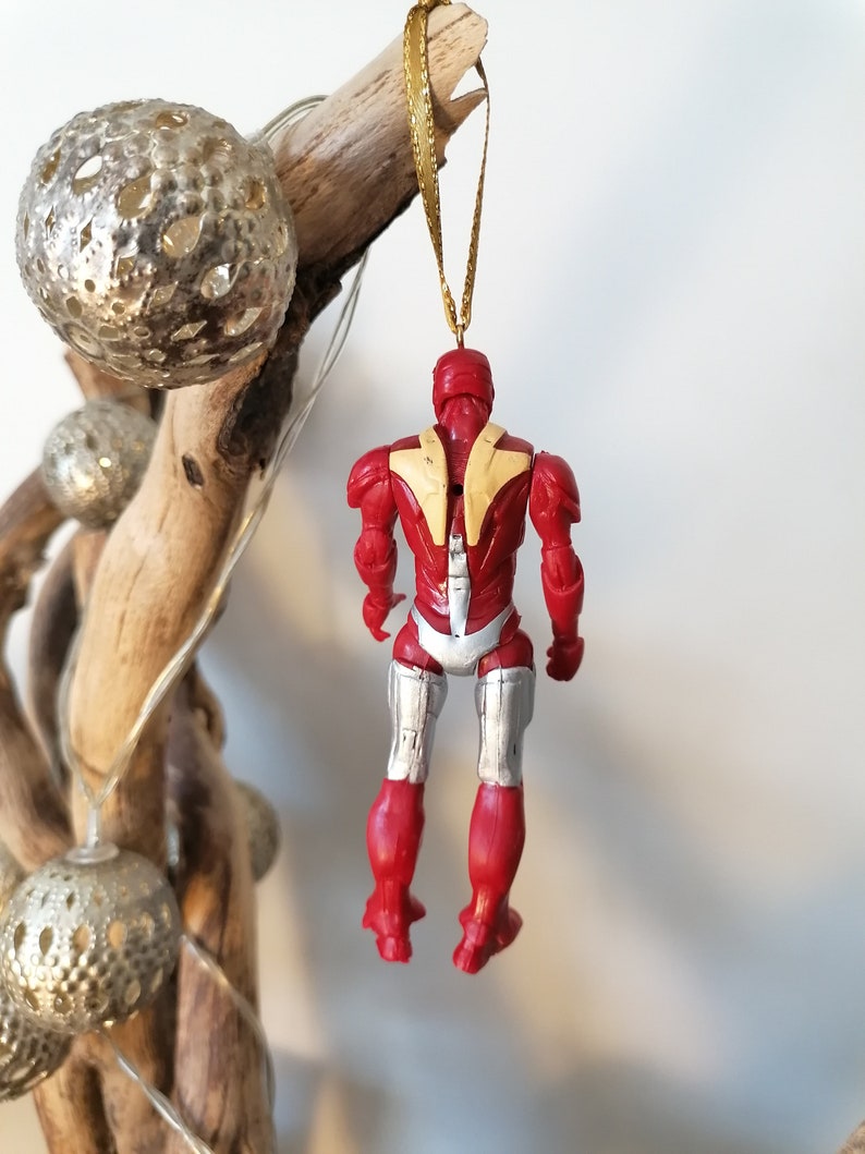 Pode incluir: Enfeite de Natal vermelho e prateado com uma figura de super-her&oacute;i e uma fita dourada.