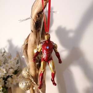 May include: A red and gold Iron Man figurine ornament hanging from a red ribbon on a piece of driftwood.