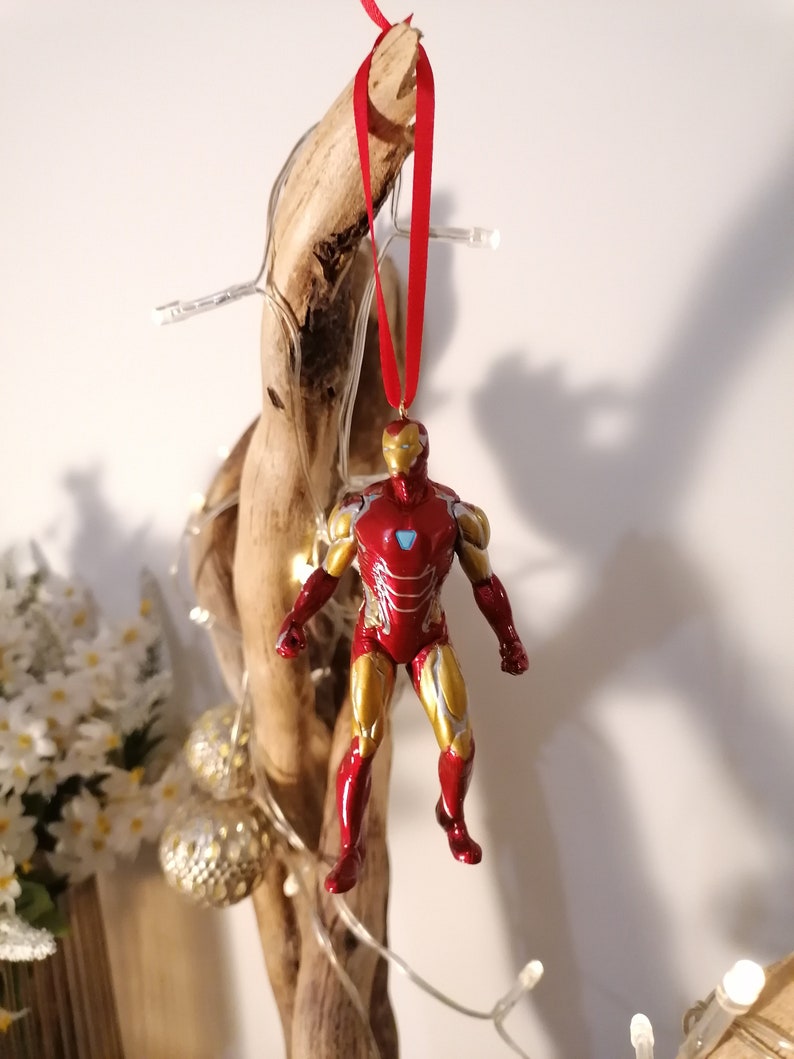 May include: A red and gold Iron Man figurine ornament hanging from a red ribbon on a piece of driftwood.