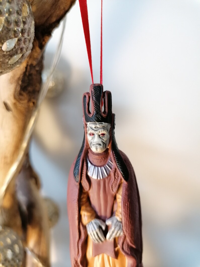 May include: A red and black Christmas ornament featuring a character from Star Wars. The character is wearing a red robe and a black crown. The ornament is hanging from a red ribbon.