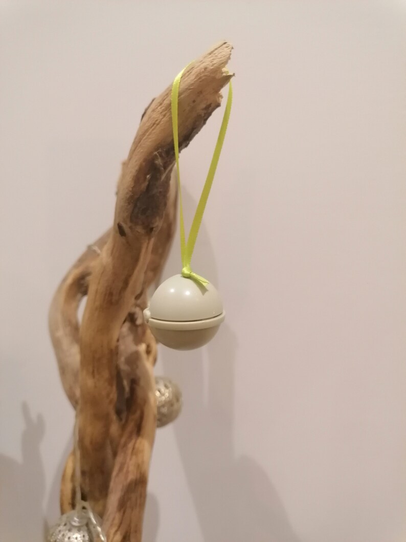 May include: A light gray, spherical ornament suspended by a bright yellow ribbon. The ornament is hanging from a piece of driftwood. Other silver ornaments are visible in the background.