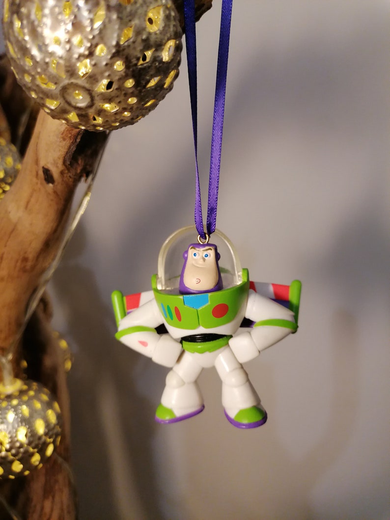 Puede incluir: Un adorno de juguete de pl&aacute;stico morado y verde de Buzz Lightyear de la franquicia de pel&iacute;culas Toy Story. El adorno est&aacute; colgado de una cinta morada.