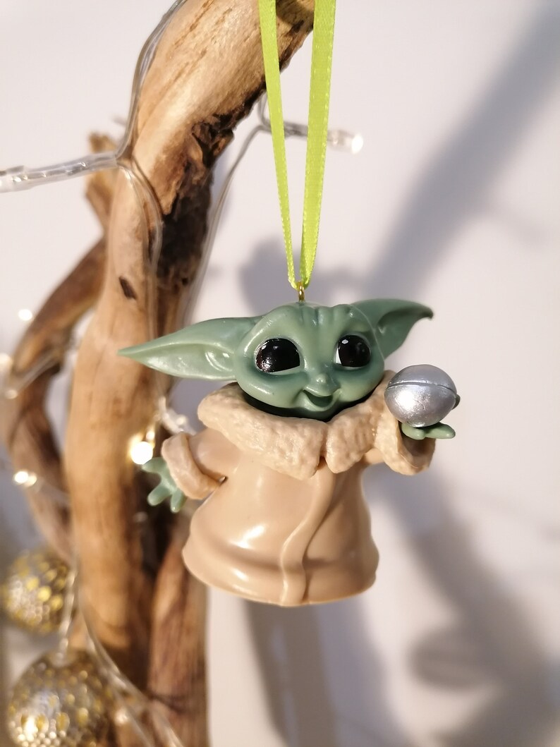 May include: A green and brown Christmas ornament featuring a character from the Star Wars franchise, holding a silver ball.