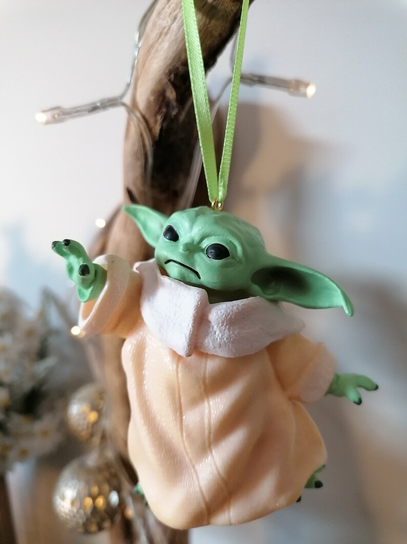 May include: A green and beige Christmas ornament featuring a character from the Star Wars franchise. The character is wearing a beige robe with a white collar and has large ears.