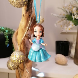 May include: A blue and white plastic doll with brown hair and a blue dress hanging from a blue ribbon.