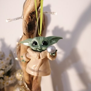 May include: A green and brown Christmas ornament featuring a character from the Star Wars franchise, holding a silver ball.