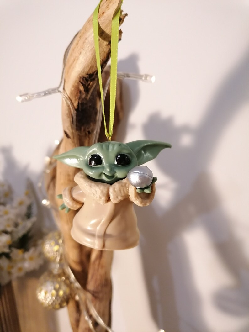 May include: A green and brown Christmas ornament featuring a character from the Star Wars franchise, holding a silver ball.