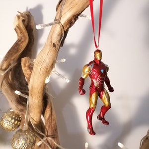 May include: Red and gold Iron Man Christmas ornament hanging from a branch with white lights.