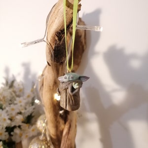 Pu&ograve; includere: Una statuetta verde e marrone di un personaggio della saga di Star Wars appesa a un pezzo di legno di deriva con un nastro verde.
