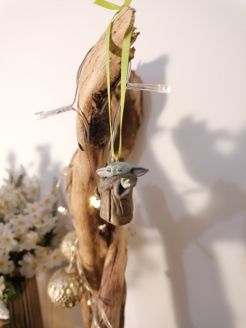 Pu&ograve; includere: Una statuetta verde e marrone di un personaggio della saga di Star Wars appesa a un pezzo di legno di deriva con un nastro verde.