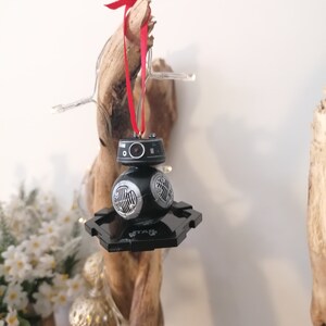 K&ouml;nnte beinhalten: Schwarzer und silberner Star Wars BB-8 Weihnachtsbaumschmuck mit einem roten Band, das an einem St&uuml;ck Treibholz h&auml;ngt.